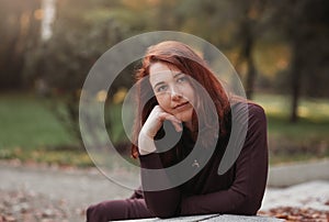 An attractive young woman with a sad pensive expression in a park on a sunny day. Shallow depth of field female creative portrait