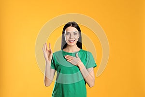 Attractive young woman showing hello gesture on yellow