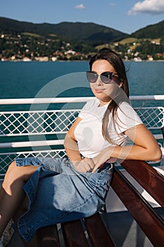Attractive young woman sitting on bench during the excursion along the lake on ship