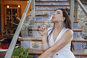 Attractive young woman is sitting on terrace steps of house and drinking champagne