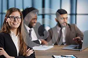 Attractive young woman smiling at camera while sitting together with another people at the table