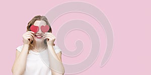 Attractive young woman smiling, having small red hearts in hands on pink background. Closing eyes with paper hearts