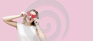Attractive young woman smiling, having small red hearts in hands on pink background. Closing eyes with paper hearts