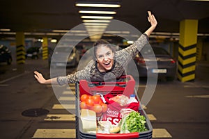 Attractive young woman smiling and pushing a shopping cart at supermarket parking lot.Concept of sale,discount,low prices