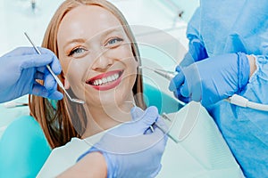 Attractive young woman smilling with natural white teeth in dental clinic. Hands doctor dentist with medical tools. Healthy teeth