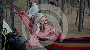 Attractive young woman speaking on mobile phone enjoying leisure time in hammock in autumn woods