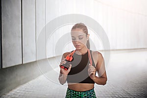 Attractive young woman in sports uniform stands and looks down. She holds orange rope around neck. Young woman is fit