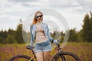 Attractive young woman in sportswear in a flower field with bike