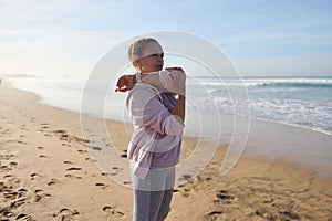 Attractive young woman in sportswear, stretching arms, warming up her body, performing bodyweight workout on the beach