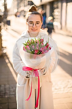 Attractive young woman with spring tulips flowers bouquet at city street