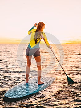 Attractive young woman stand up paddle surfing with beautiful sunset or sunrise colors