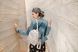 Attractive young woman standing between concrete walls. Caucasian girl in casual jeans and dress