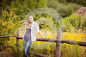 Attractive young woman standing near old wooden fence.