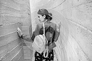 Attractive young woman stands between concrete walls. Caucasian girl in casual jeans and dress looks back