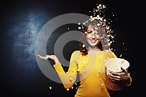 Attractive young woman staying under popcorn shower with hand up