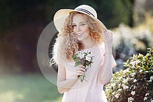 Attractive young woman in a straw hat alone in a blooming spring park