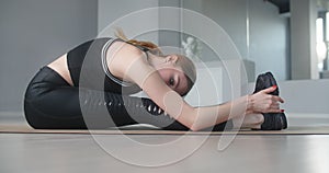Attractive young woman stretches herself by bending forward in sitting position on the floor on the youga mat, yoga