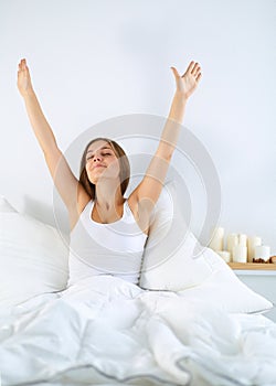 Attractive young woman stretching in bed after waking up