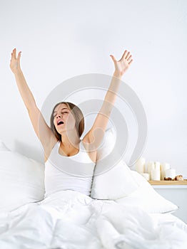 Attractive young woman stretching in bed after waking up