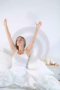 An attractive young woman stretching in bed after waking up.