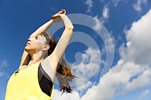 Attractive young woman stretching her arms while standing against a deep blue sky, exercising on a sunny day