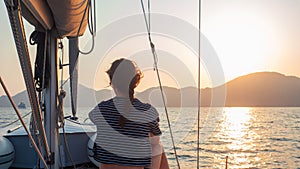 Attractive young woman in a striped t-shirt enjoys the sunset on the deck of a sailing yacht.