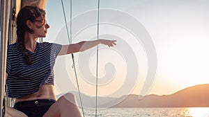 Attractive young woman in a striped t-shirt enjoys the sunset on the deck of a sailing yacht. Girl yachtsman