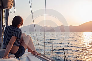 Attractive young woman in a striped t-shirt enjoys the sunset on the deck of a sailing yacht. Girl yachtsman