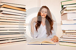Attractive young woman studies wtih huge book piles on her desk