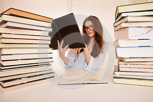 Attractive young woman studies wtih hugr book piles on her desk