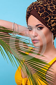 An attractive young woman in a stylish turban made of leopard print fabric on a blue background.
