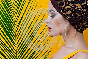 An attractive young woman in a stylish turban made of leopard print fabric on a yellow mango background.