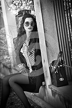 Attractive young woman with sunglasses in autumnal fashion shot. Beautiful lady in black and white outfit with short skirt sitting