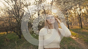 Attractive young woman in sweater, jeans is dance and spinning among blossom apple tree. Sunset, spring orchard and