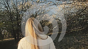 Attractive young woman in sweater, jeans is dance and spinning among blossom apple tree. Sunset, spring orchard and