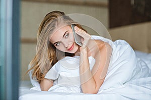 Attractive young woman talking on mobile phone lying in bed