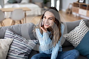 Attractive young woman talking on phone and smiling while sitting on a sofa at home