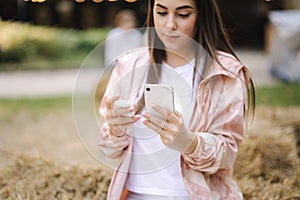 Attractive young woman try to conect witeless headphones to her phone. Woman sitting on hay bench in cafe outdoors