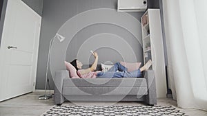 Attractive young woman typing on her smart phone while lying on the sofa at home. Smilling woman using smart phone