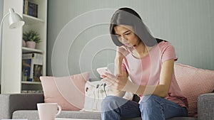 Attractive young woman typing on her smart phone while sitting on the sofa at home.