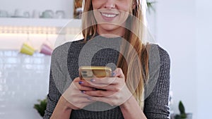 Attractive young woman using her mobile phone while eating a salad in the kitchen at home.