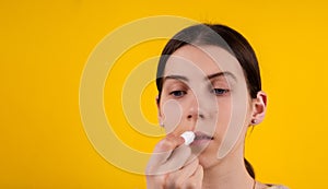 Attractive young woman using hygienic lipstick on yellow background. lips care and protection. woman applying balm on lips