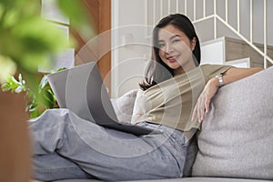 Attractive young woman using laptop computer while resting on comfortable couch at home