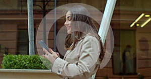 Attractive young woman using phone walking near Big Modern Office Building. Chatting with friends, girl using cellphone