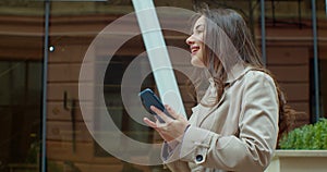 Attractive young woman using phone walking near Big Modern Office Building. Chatting with friends, girl using cellphone