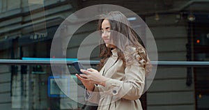 Attractive young woman using phone walking near Big Modern Office Building. Chatting with friends, girl using cellphone