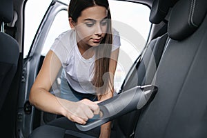 Attractive young woman using portable vacuum cleaner in her car. Woman vacuuming her car in the garage at home. Car