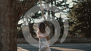 Attractive young woman walking at park near the road at sunset. Female enjoying the bright spring day, explore the city.