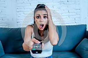 Attractive young woman watching a scary movie alone at home looking horrified