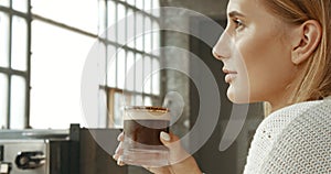 Attractive young woman wearing a white sweater in a loft style bakery or coffee shop with an ice latte